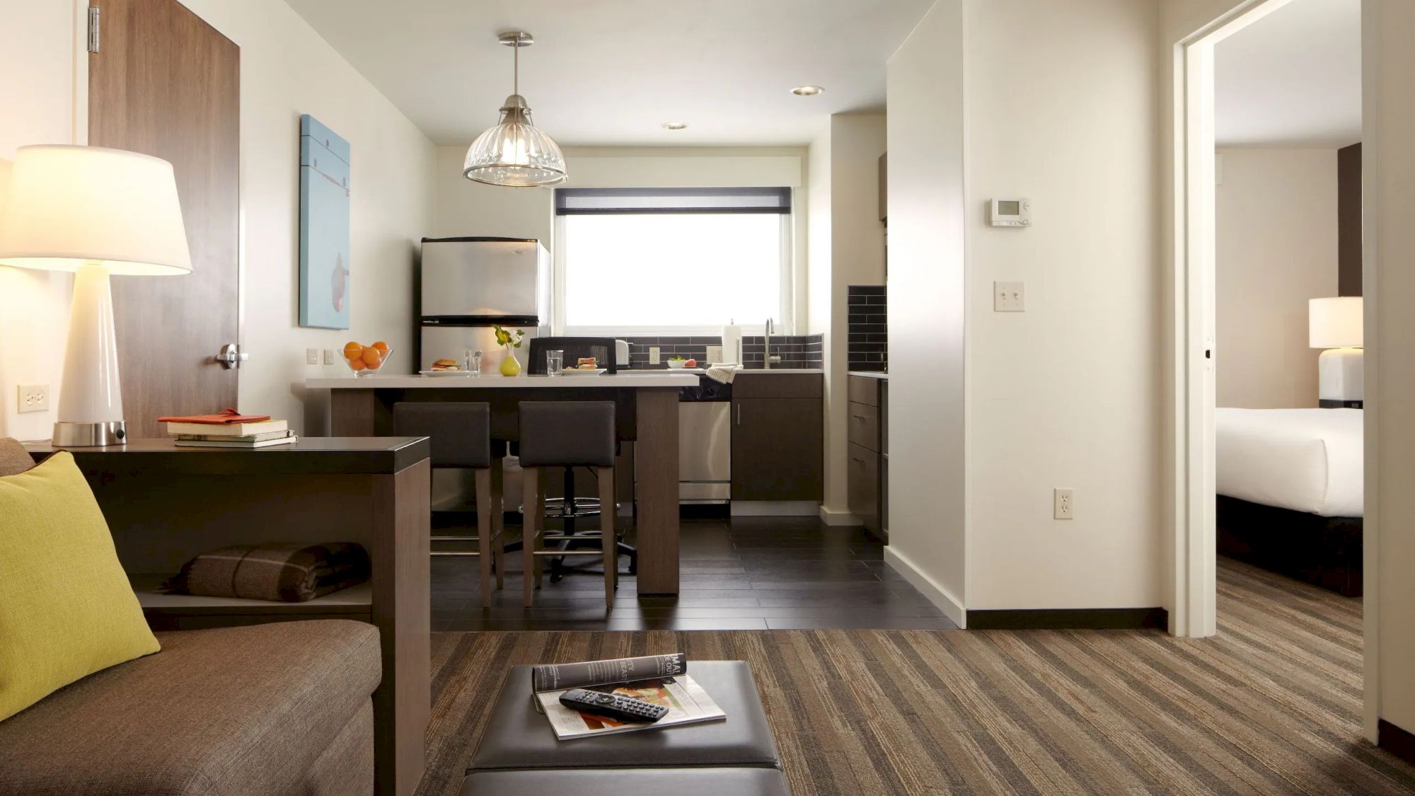 This image shows a modern, compact living space with a sofa, dining table, kitchen area, and a bedroom. The decor is minimalist and cozy.