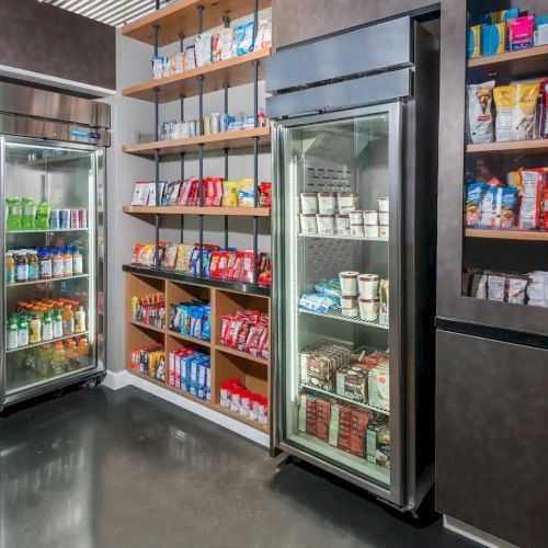 The image shows a well-stocked snack and beverage area with refrigerated units containing various drinks and shelves filled with snacks.