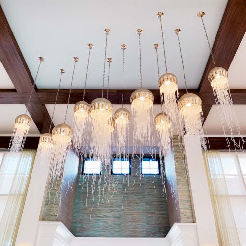 The image shows a modern interior with a high ceiling, featuring elegant chandeliers that have long, dangling elements, creating a luxurious atmosphere.