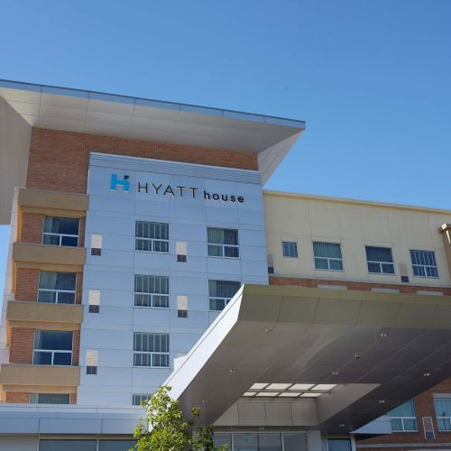 The image shows the exterior of a Hyatt House hotel building under a clear blue sky.