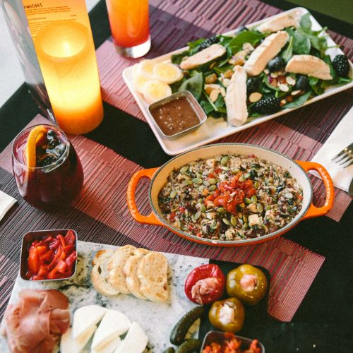 A table with various dishes: salad, mixed rice, charcuterie, plus drinks and candles, set in a cozy dining atmosphere.