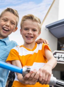 Two boys smiling and holding a toy lightsaber in front of the Star Wars Launch Bay attraction.