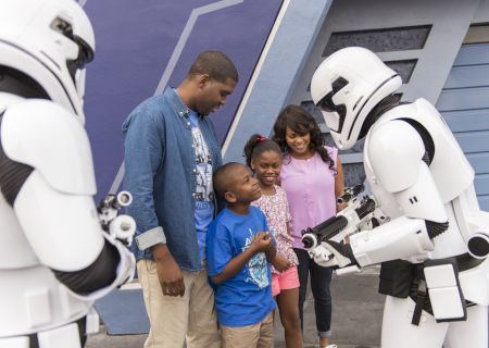 A family interacts with two people in Stormtrooper costumes at a theme park or event, engaging joyfully and taking photographs.