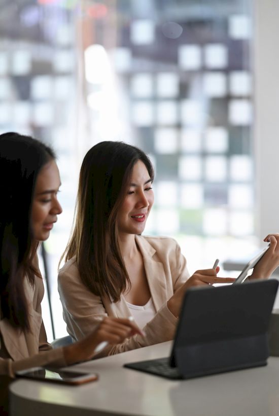 Two people are sitting at a table, engaging with a laptop in a bright, modern space.