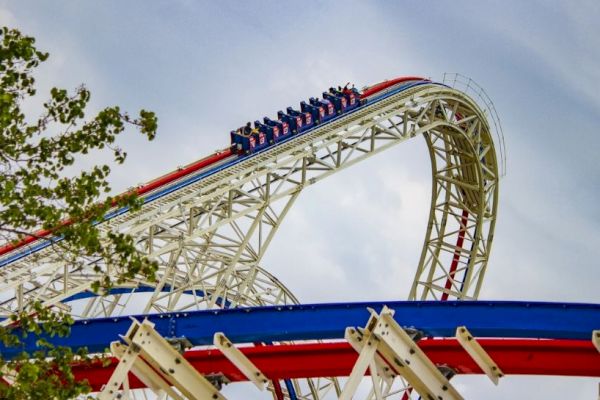 A roller coaster is captured mid-loop with people riding, against a partly cloudy sky and some trees in the foreground.